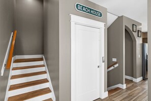 A hallway with a staircase, a white door, and a sign that reads "BEACH HOUSE".
