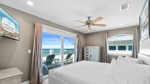 A bedroom with a bed, a ceiling fan, a window with curtains, a view of the ocean, and a sign on the wall. - Beachfront Duplex Unit, Pet Friendly, Mexico Beach, Gorgeous Views! (Mexico Beach)
