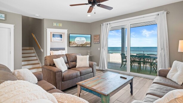 A living room with a brown leather sofa, a wooden coffee table, and a ceiling fan. There is a large window with a view of the ocean and a patio with outdoor furniture. - Beachfront Duplex Unit, Pet Friendly, Mexico Beach, Gorgeous Views! (Mexico Beach)