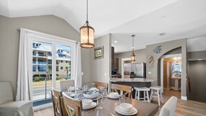 A dining area with a table set for four, a kitchen in the background, and a view of a residential building through a glass door. - Beachfront Duplex Unit, Pet Friendly, Mexico Beach, Gorgeous Views! (Mexico Beach)
