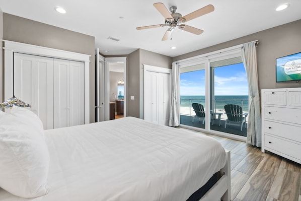 A bedroom with a bed, a ceiling fan, a TV, and a view of the ocean.