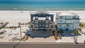 Une propriété située en bord de mer, comprenant une grande maison et un bâtiment plus petit, tous deux dotés de nombreuses fenêtres et d’un abri-voiture.
