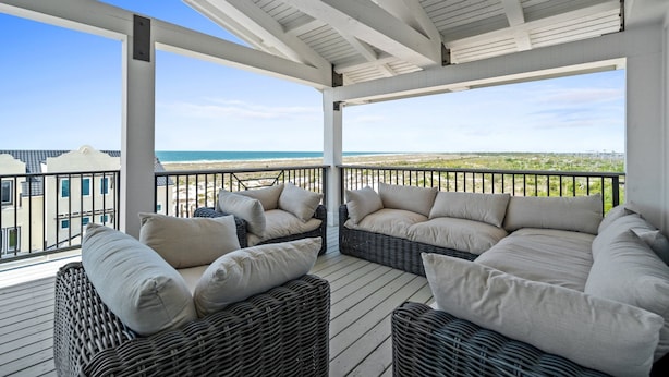 A covered outdoor seating area with wicker furniture and cushions, overlooking a beach and ocean. - Estate Home: Gulf Views, Private Pool, Pool Table, Sleeps 20! (Mexico Beach)