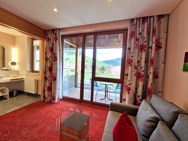 A modern hotel room with a balcony, a sofa, a small table, and a bathroom with a mirror and sink. - Mosers Blume Relax & Genuss Hotel (Haslach im Kinzigtal)