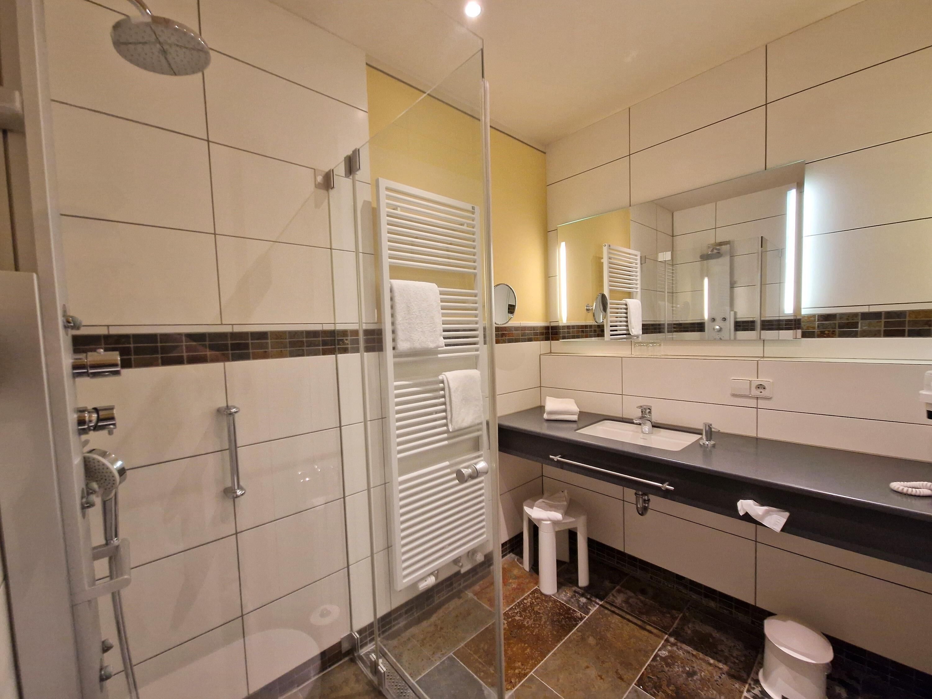 A modern bathroom with a glass-enclosed shower, a large mirror, a sink with a vanity, and a toilet.