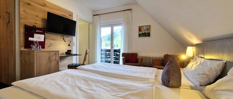A bedroom with a large bed, a TV mounted on a wooden wall, a desk with a chair, and a window with a view of the outdoors.