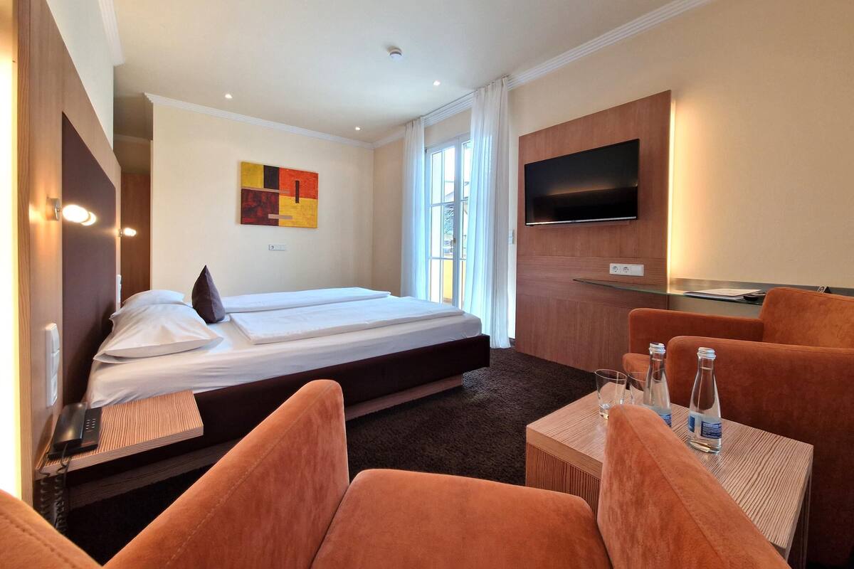 Ein Hotelzimmer mit Bett, Fernseher, Schreibtisch und orangenen Stühlen.