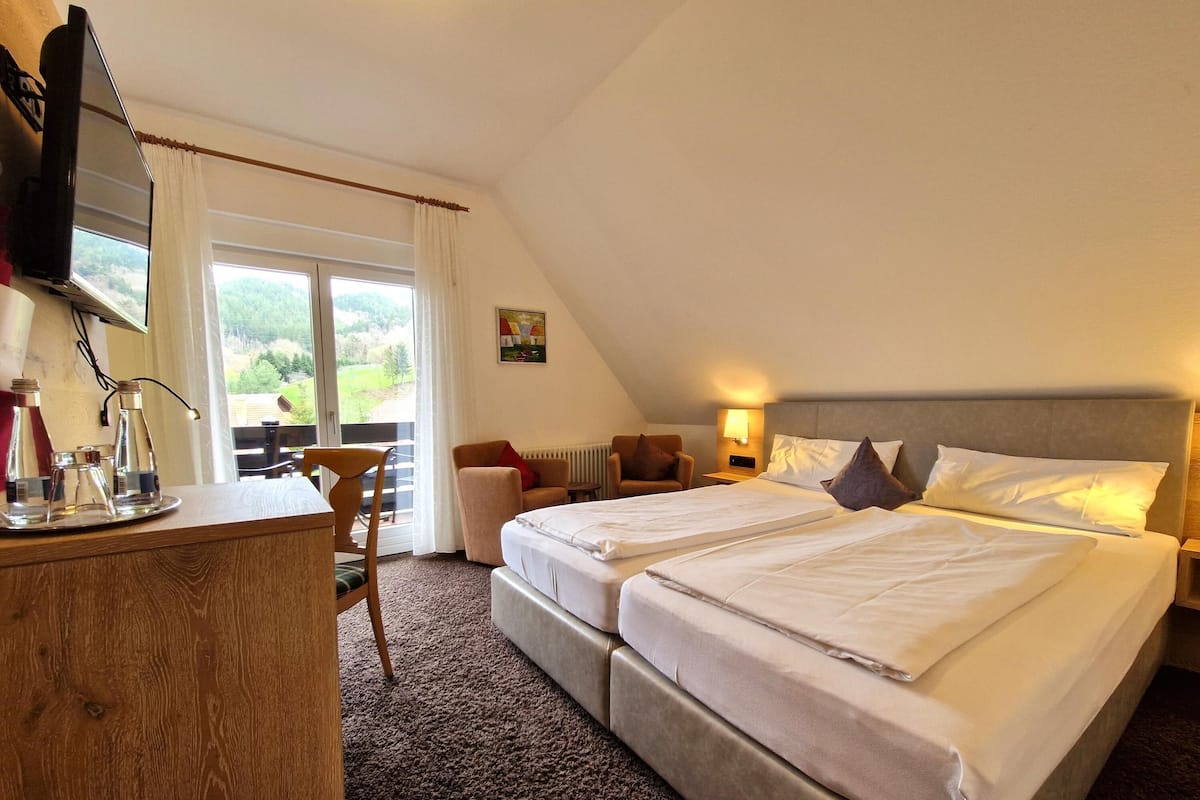 Ein Hotelzimmer mit zwei Betten, einem Schreibtisch, einem Stuhl, einem Heizkörper und einem Fenster mit Vorhängen.