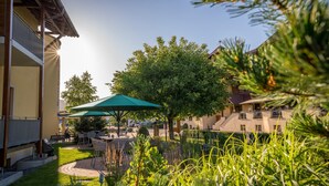 A courtyard with outdoor seating, a green umbrella, and a building with a balcony. - Mosers Blume Relax & Genuss Hotel (Haslach im Kinzigtal)