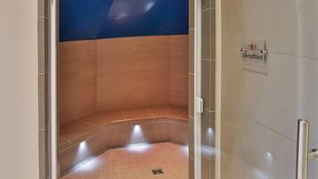 Relax in a serene sauna room with a tiled floor and walls, featuring a bench and a clear glass door.