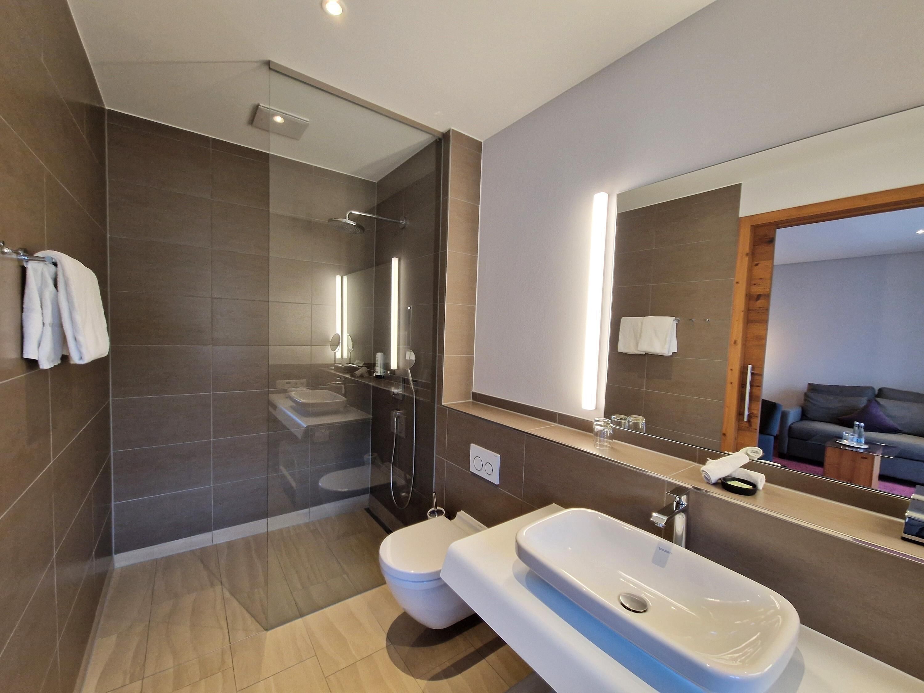Une salle de bain moderne avec une douche à parois de verre, des toilettes blanches et un grand miroir.