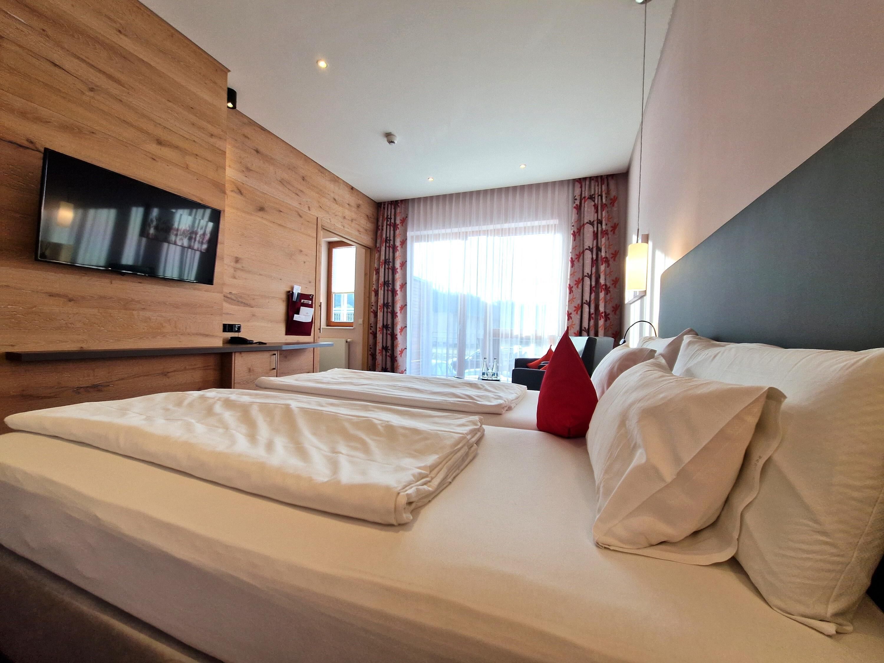 Una habitación de hotel con una cama grande, un televisor montado en la pared y una ventana con cortinas.