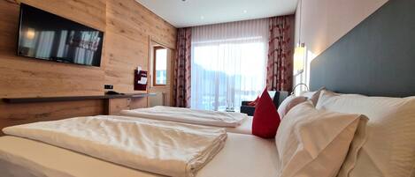Una habitación de hotel con una cama grande, un televisor montado en la pared y una ventana con cortinas.