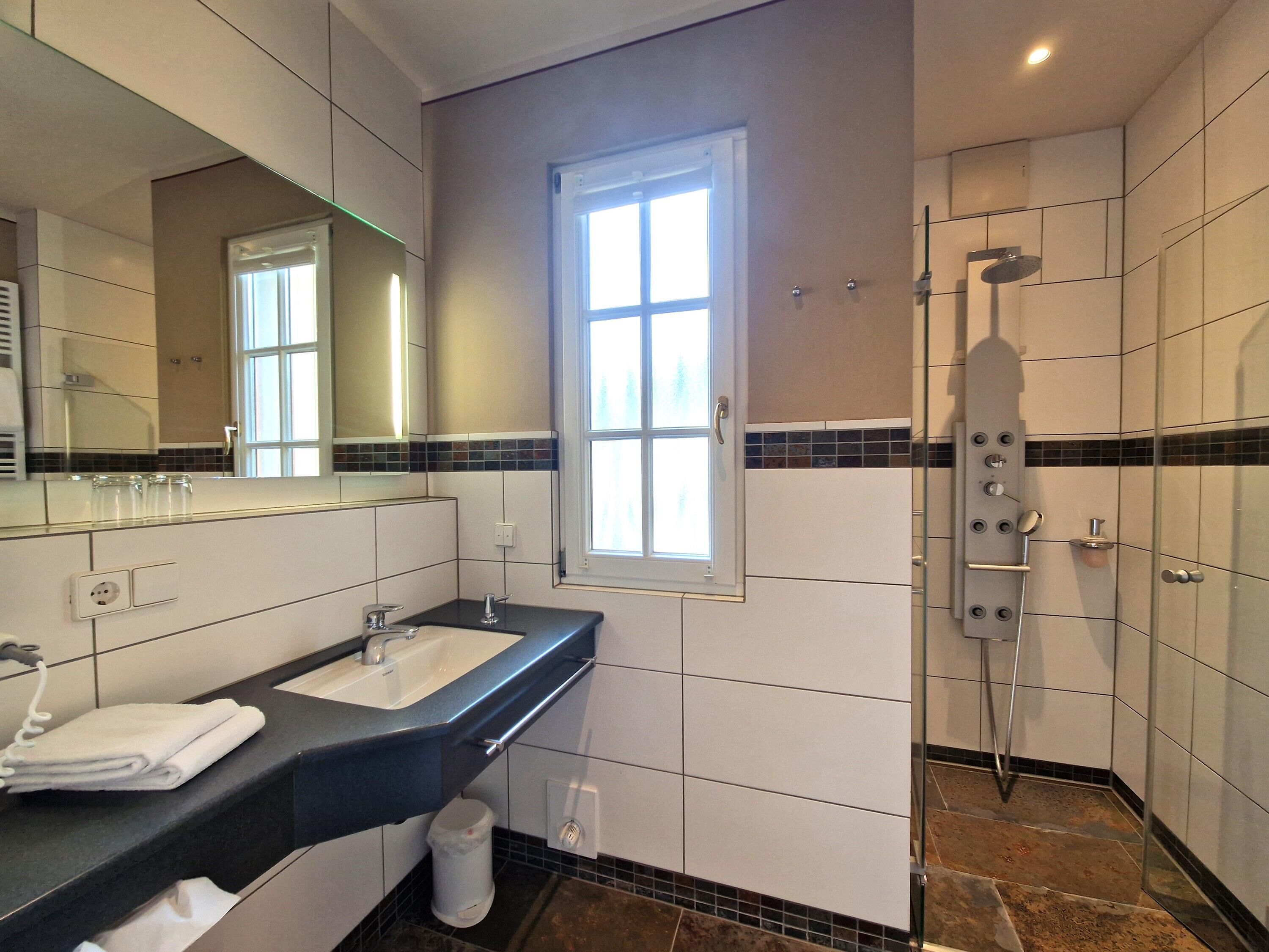 Un baño moderno con un espejo grande, un lavamanos, una ducha y una ventana.