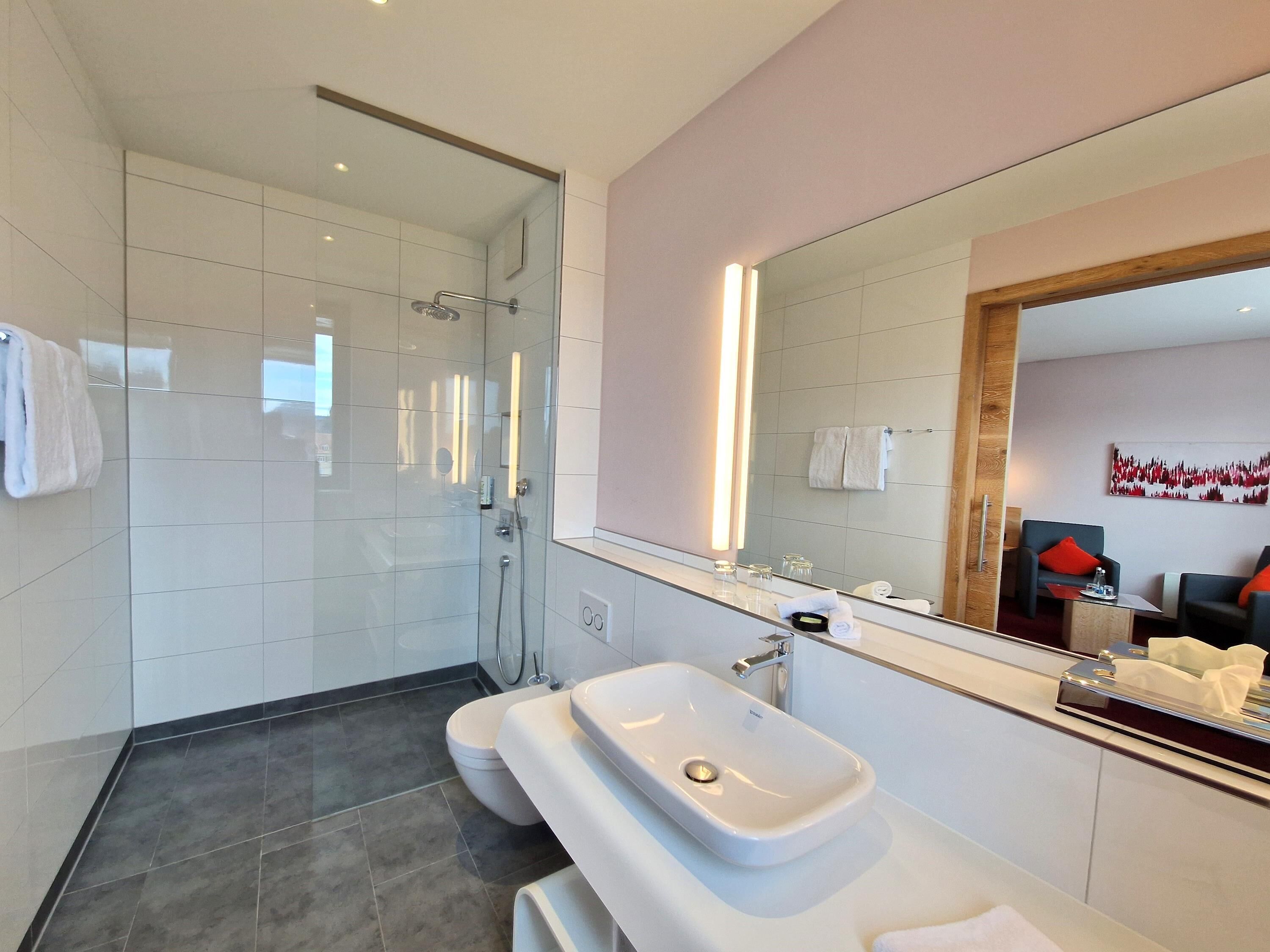 Un baño moderno con ducha envuelta en vidrio, un lavabo blanco y un espejo grande.