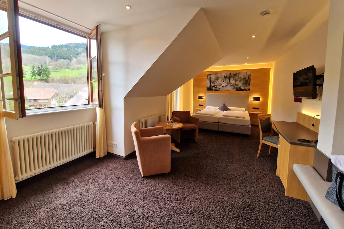 Ein Hotelzimmer mit großem Fenster, einem Bett, einem Schreibtisch und einem Stuhl.