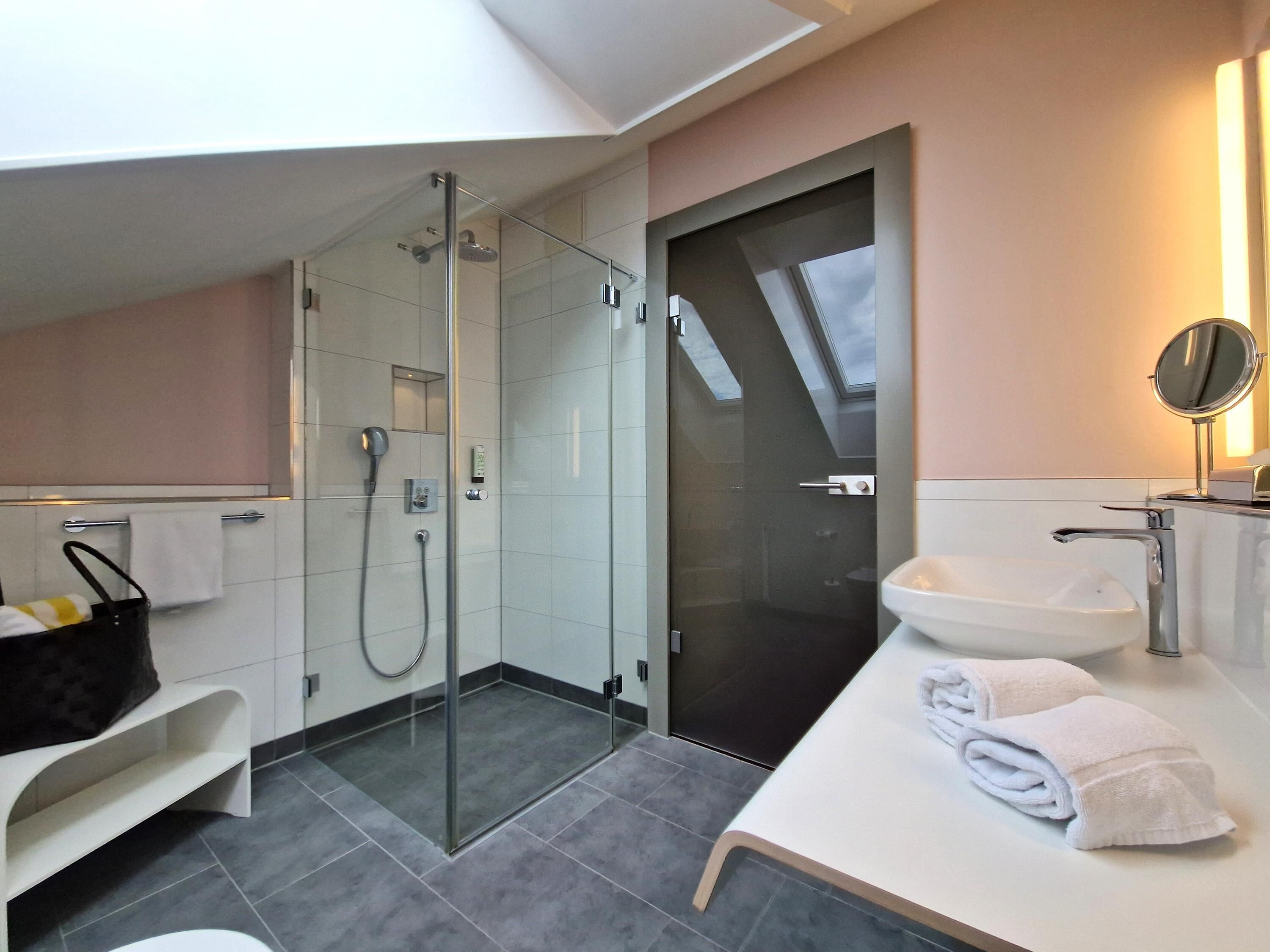 Un baño moderno con ducha envuelta en vidrio, un lavabo blanco y un tocador con espejo.