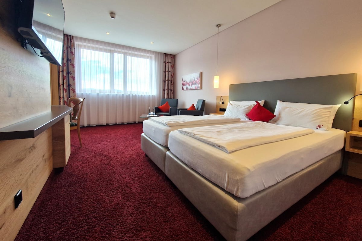 Ein Hotelzimmer mit einem großen Bett, einem Schreibtisch, einem Stuhl und einem an der Wand befestigten Fernseher.