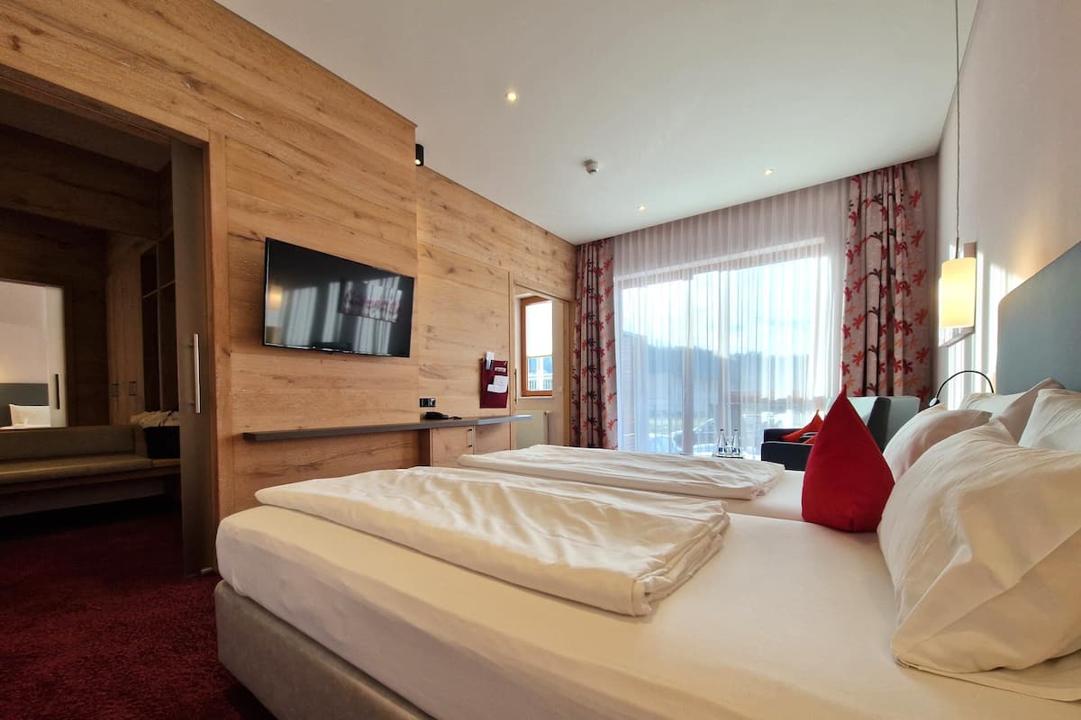 Ein Hotelzimmer mit einem großen Bett, einem an der Wand befestigten Fernseher, einem Schreibtisch und einem Fenster mit Vorhängen.