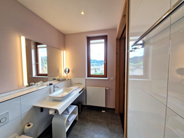 A modern bathroom with a large mirror, a sink, and a window providing a view of buildings outside. - Mosers Blume Relax & Genuss Hotel (Haslach im Kinzigtal)