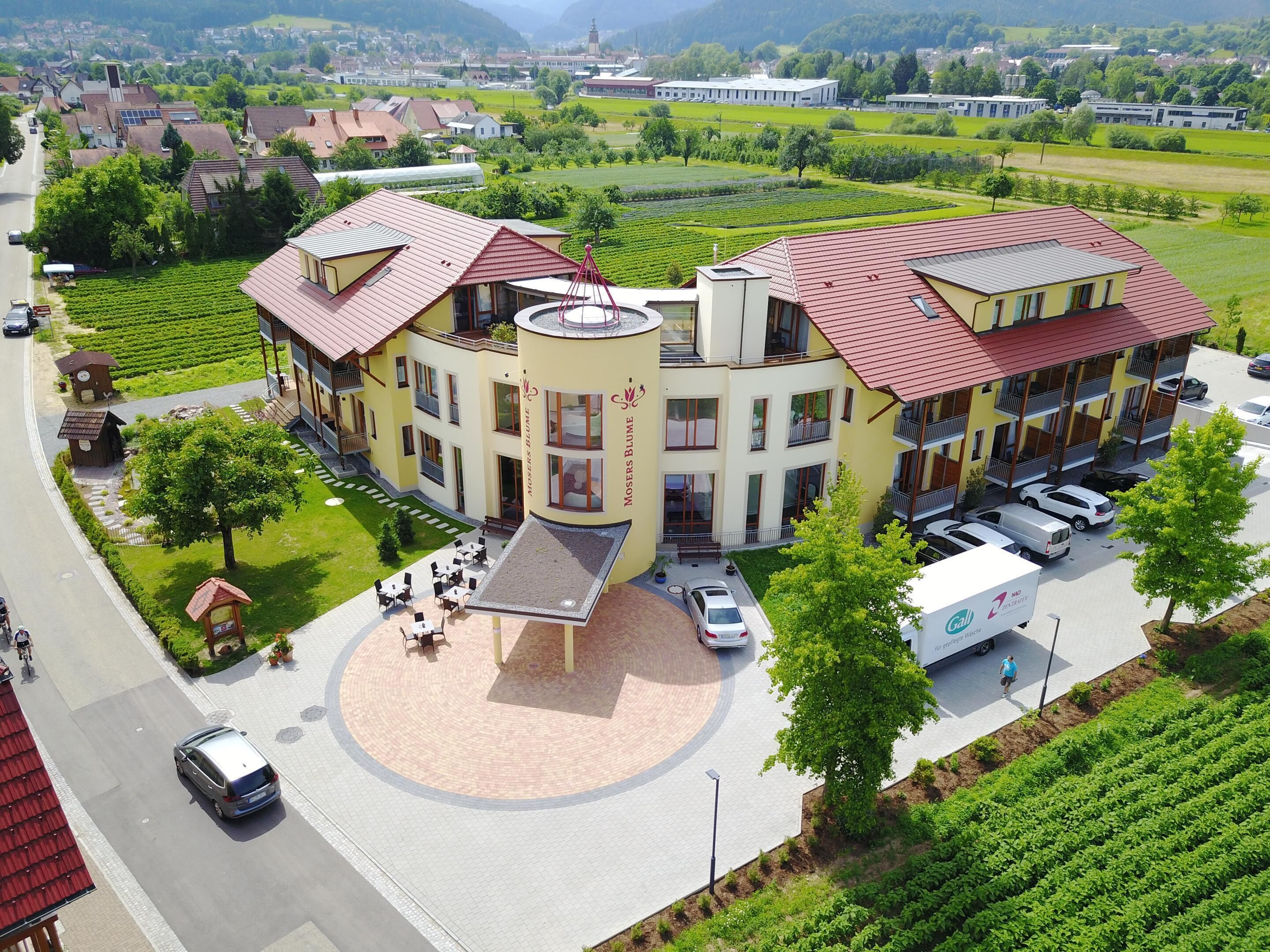A multi-story building with a central courtyard, surrounded by green fields and a road.