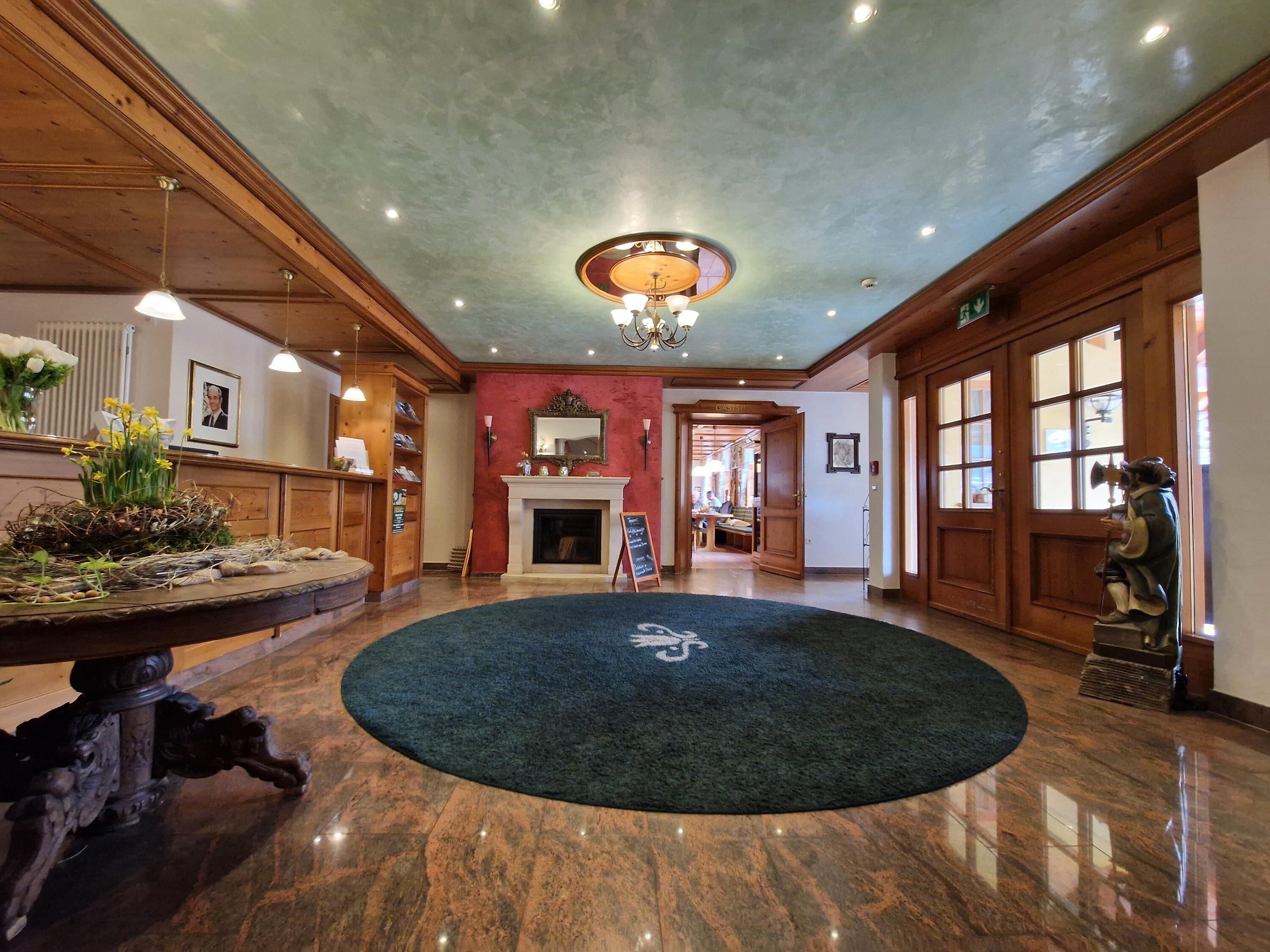 Eine Lobby mit Kamin, einem runden Teppich mit Logo, Holzvertäfelung und einer Chandelier.
