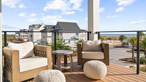 Ein Balkon mit Gartenmöbeln, Blick auf den Strand und ein Gebäude im Hintergrund.