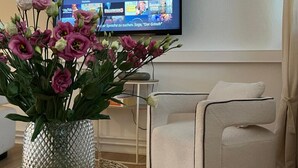 A living room with a flat-screen TV mounted on the wall displaying a streaming service interface. In the foreground, there is a vase with pink flowers on a woven tray. - Vacation apartment with wellness - in the heart of Worms! (Worms)