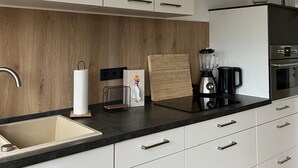 A modern kitchen with white cabinets, a wooden backsplash, a sink, a coffee maker, and a blender on the countertop. - Vacation apartment with wellness - in the heart of Worms! (Worms)