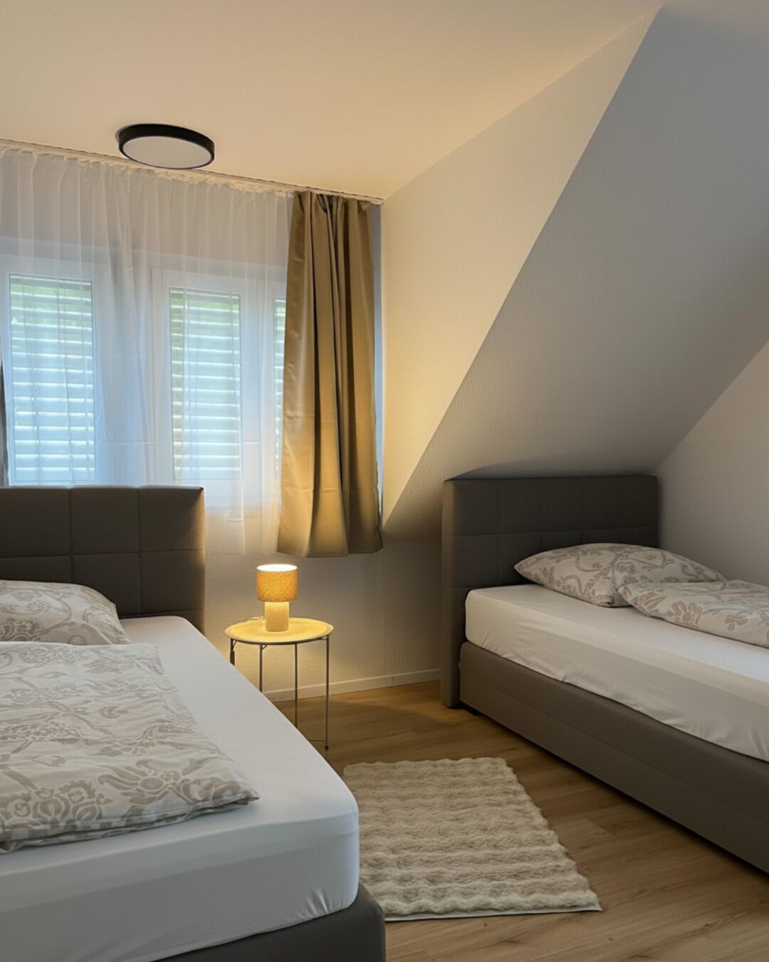 Un dormitorio con dos camas, una mesita de noche con lámpara y una ventana con cortinas.