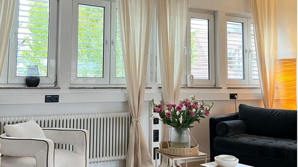 A modern living room with a white radiator, a black sofa, a white armchair, and a small table with a vase of flowers. - Vacation apartment with wellness - in the heart of Worms! (Worms)