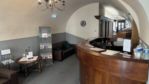Une salle d’attente avec un bureau en bois, un canapé, un lustre, un tableau d’affichage et une horloge au mur.