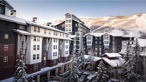 Un hôtel à plusieurs étages, doté d’une architecture moderne, avec une façade aux couleurs contrastées, mêlant le rouge et le blanc, et entouré d’arbres couverts de neige.
