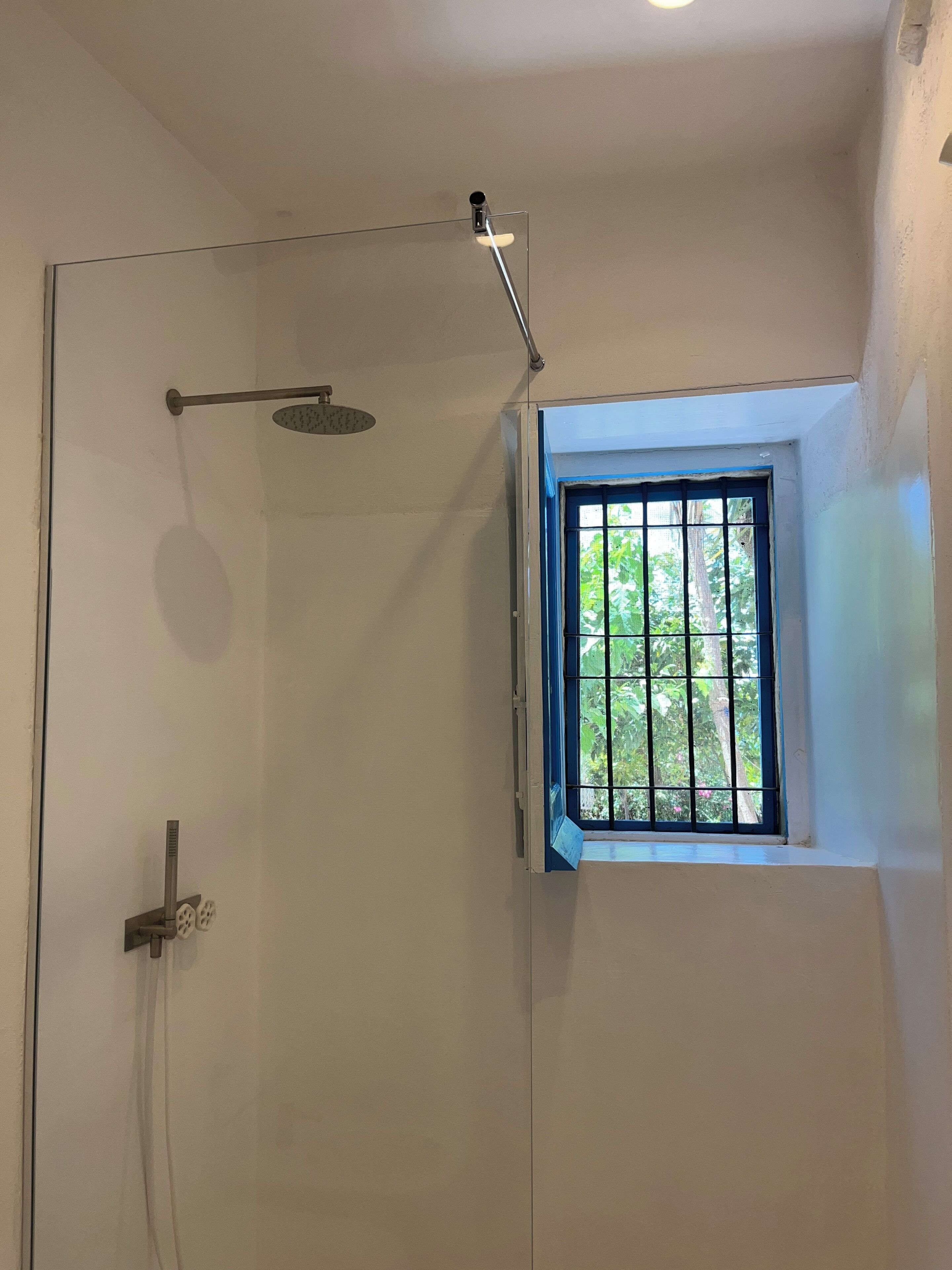 A shower with a rain showerhead and a window with metal bars.