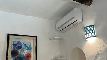 Ein Zimmer mit weißer Wand, einem gerahmten abstrakten Gemälde, einer weißen Klimaanlage, einer kleinen Ablage mit zwei Schalen und einer dekorativen Leuchte.