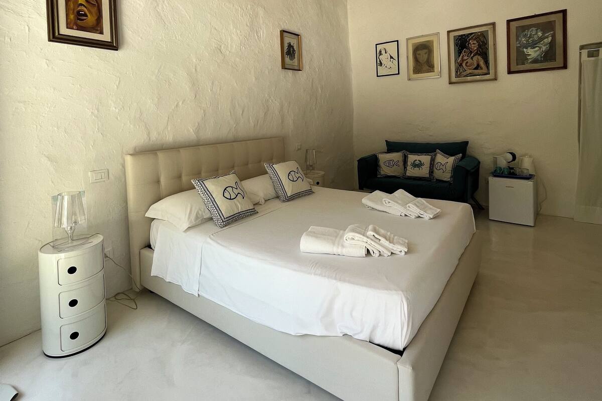 A spacious bedroom with a large bed, a nightstand, a dresser, and a chandelier.