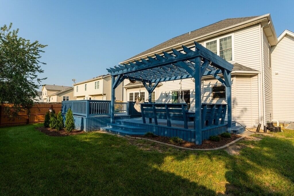 Eine blaue Pergola mit Stufen, die zu einer überdachten Terrasse im Garten eines Wohnhauses führen.
