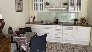 A modern kitchen with white cabinetry, a coffee machine, and a dining area with a table and chairs. - Enjoy KRK waterfalls, sun, beach and sea: Domicile Sunce Kornati (Skradin)