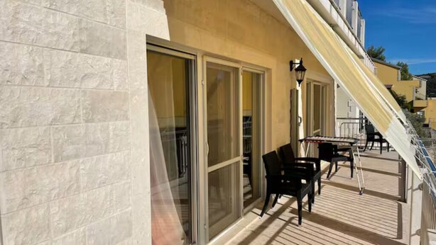 A sunlit outdoor area with a wooden deck, a table with chairs, and a building with large sliding glass doors. - Enjoy KRK waterfalls, sun, beach and sea: Domicile Sunce Kornati (Skradin)