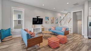 A modern living room with a blue sofa, a wooden coffee table, and striped ottomans. - Beach Retreat | Pool + Steps to Sand (Gulf Shores)