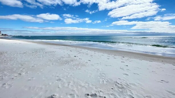 A beach with white sand and a clear blue sky with scattered clouds. - Beach Retreat | Pool + Steps to Sand (Gulf Shores)