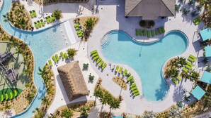Un resort con una piscina centrale, diverse zone relax con lettini prendisole e un edificio con tetto di paglia.