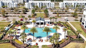 Un hotel con piscina centrale circondata da palme e lettini, con diversi edifici sullo sfondo.