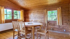A wooden cabin with a dining table and chairs, large windows with curtains, and a wooden ceiling. - Comfortable Home With Terrace (Masserberg)