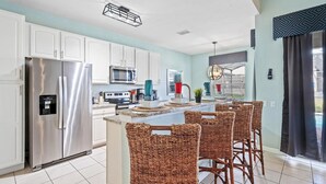 A modern kitchen with white cabinets, stainless steel appliances, a central island with bar stools, and a view of the outdoors through large windows. - Closest resort to Disney/Private Pool and Hot Tub/Gated Community/FreeWifi (Kissimmee)