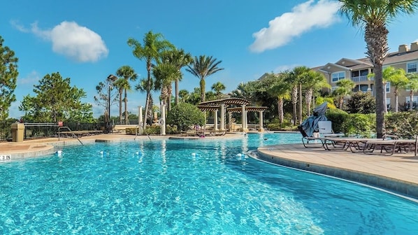 A swimming pool with lounge chairs, palm trees, and a gazebo.
