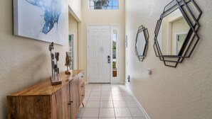 A hallway with a wooden cabinet, a large abstract painting, a white door, and geometric wall mirrors. - Closest resort to Disney/Private Pool and Hot Tub/Gated Community/FreeWifi (Kissimmee)