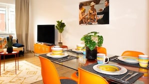 Un coin repas avec des chaises orange, une table en verre et un tableau au mur.