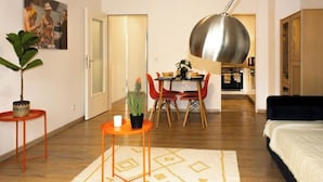 Un espace de vie compact comprenant un coin repas, une cuisine à l’arrière-plan et un grand luminaire suspendu.
