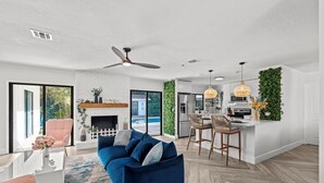 A modern living room with a blue sofa, a white fireplace, and a kitchen area with a green vertical garden.